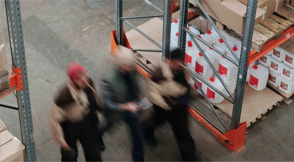 Warehouse workers walking through storage facility aisle with shelves of products