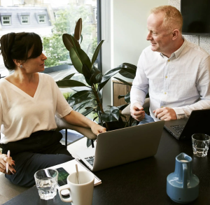 Business meeting with two professionals collaborating at a desk with laptops in an office